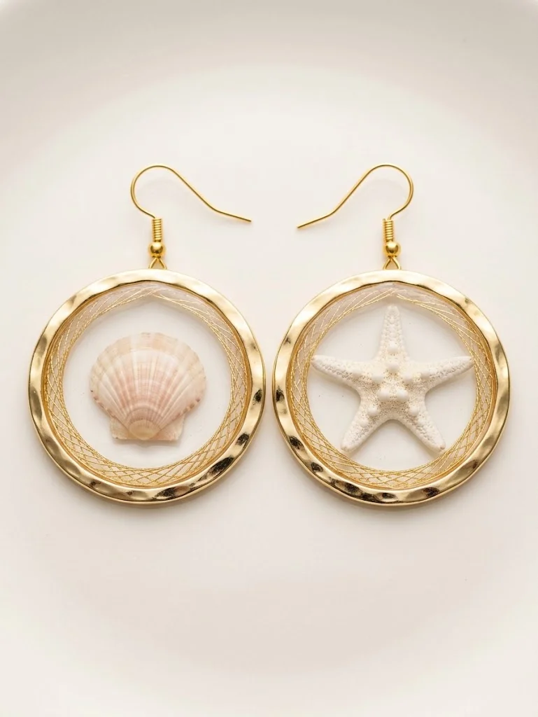 Hammered gold hoop earrings on cream, one holding a natural scallop shell and one a white starfish inside a gold thread-wrapped ring